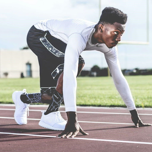 Man wearing a white shirt and black shorts on a track about to start running